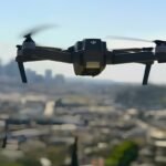 Black quadcopter drone flying against a hazy blue sky over Pune