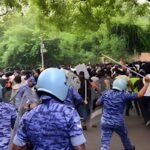 Riot police in helmets and blue camouflage uniforms facing a crowd of protesters during the July 20 Jantar Mantar demonstration