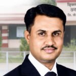 Portrait of Adv. Vikas Phadtare in a black suit with a court building in the background