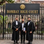 Two lawyers in black robes standing with their client in front of the Bombay High Court gate