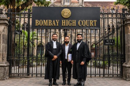 Two lawyers in black robes standing with their client in front of the Bombay High Court gate