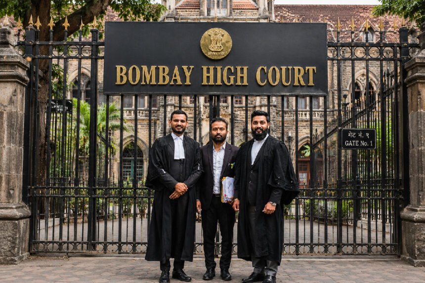 Two lawyers in black robes standing with their client in front of the Bombay High Court gate