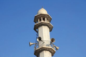 Loudspeakers mounted on a minaret tower against a blue sky