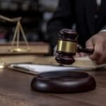A judge's hand holding a wooden gavel beside a set of justice scales on a desk