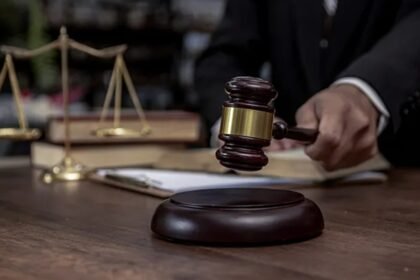 A judge's hand holding a wooden gavel beside a set of justice scales on a desk