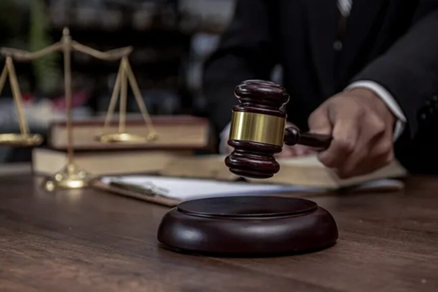 A judge's hand holding a wooden gavel beside a set of justice scales on a desk