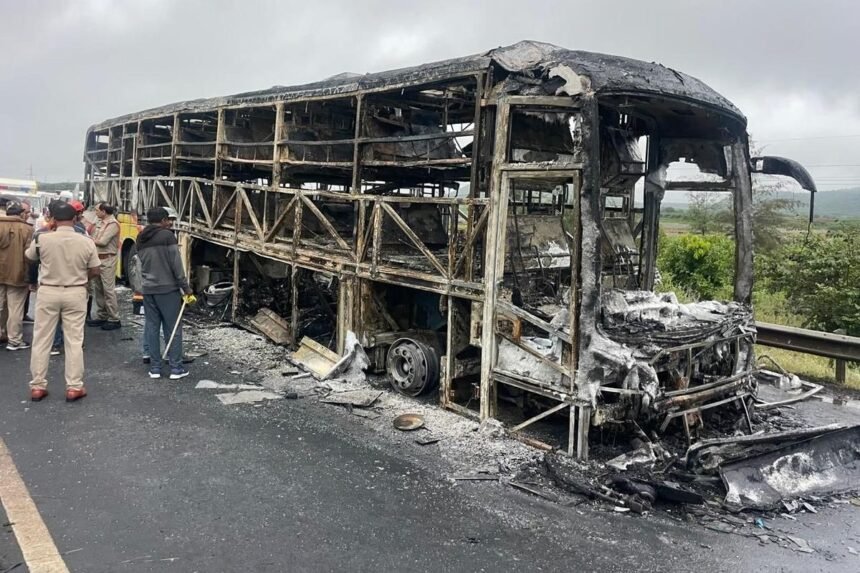 urnt-out skeleton of a bus on a roadside with officials standing nearby