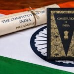 भारतीय संविधानाची उद्देशिका दर्शवणारी सुशोभित गुंडाळी आणि "Constitution of India" पुस्तक, तिरंग्याच्या पार्श्वभूमीवर