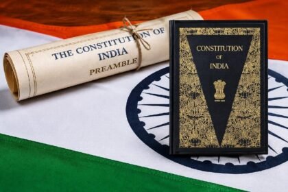 भारतीय संविधानाची उद्देशिका दर्शवणारी सुशोभित गुंडाळी आणि "Constitution of India" पुस्तक, तिरंग्याच्या पार्श्वभूमीवर