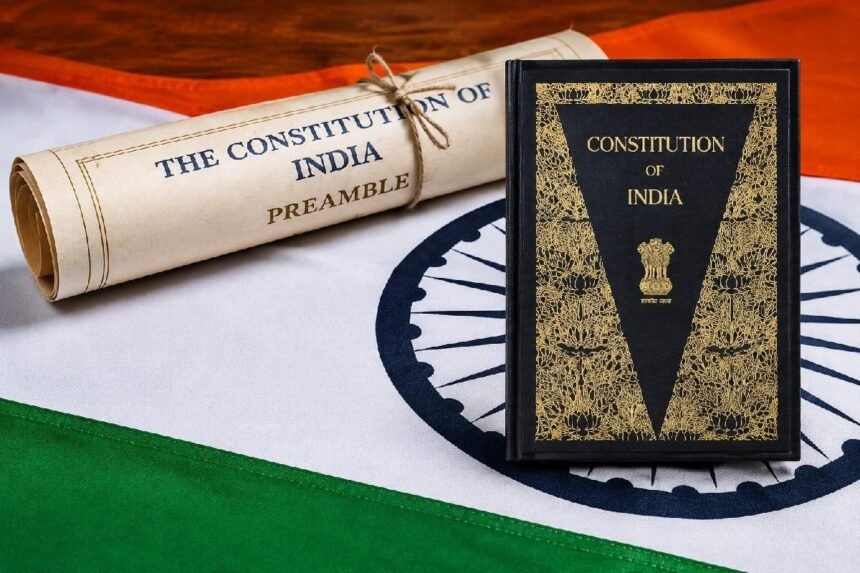 भारतीय संविधानाची उद्देशिका दर्शवणारी सुशोभित गुंडाळी आणि "Constitution of India" पुस्तक, तिरंग्याच्या पार्श्वभूमीवर
