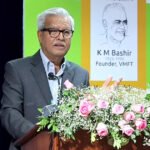 Adv. Dushyant Dave speaking at a podium during the K.M. Bashir Memorial Lecture, with a stage backdrop showing a portrait of K.M. Bashir (1925–1990) and the lecture's title displayed on screen.