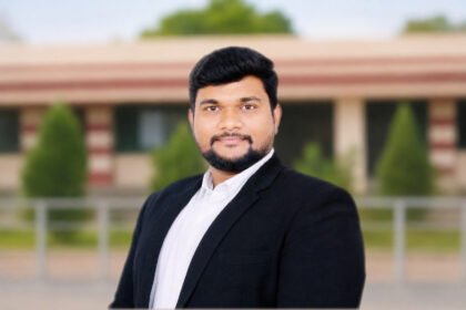 ॲड. विराज करचे यांचा औपचारिक पोर्ट्रेट फोटो, काळ्या ब्लेझरमध्ये, इमारतीसमोर उभे