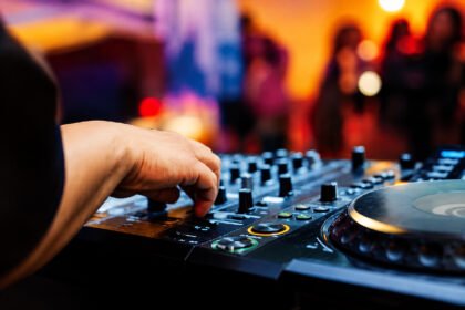 A DJ's hand adjusting a mixing console at a nighttime event with a crowd in the background