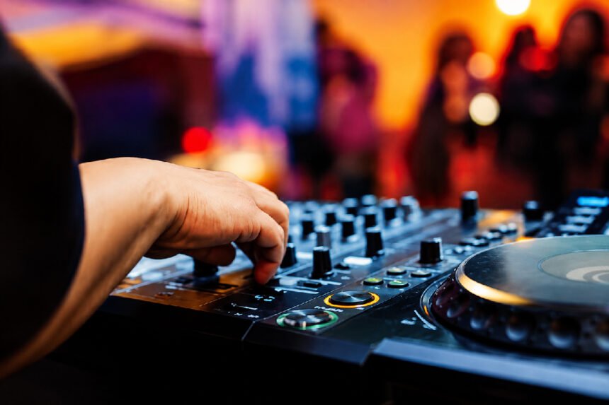 A DJ's hand adjusting a mixing console at a nighttime event with a crowd in the background