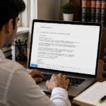 A person typing an email on a laptop at a desk with law books and a justice scale figurine